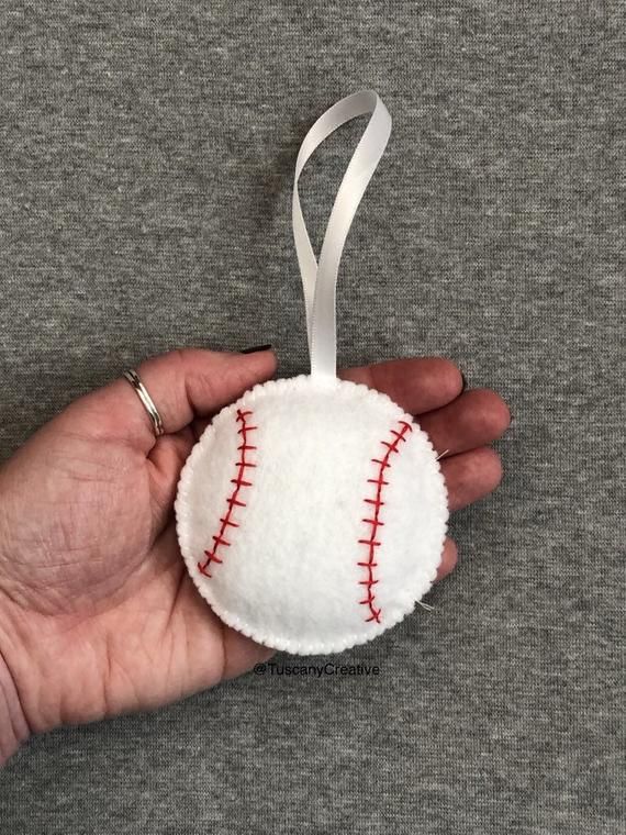 someone holding a baseball ornament in their left hand with a ribbon around it