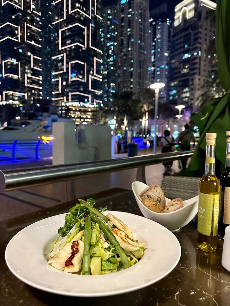 a white plate topped with food next to a bowl of salad and bottle of wine