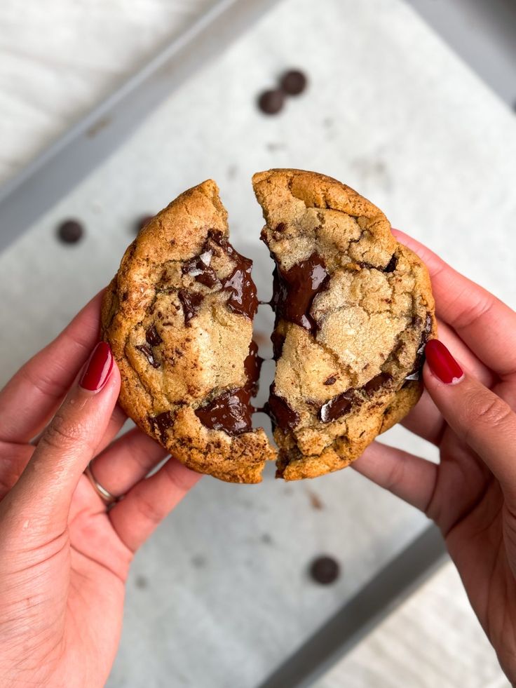 a person holding a chocolate chip cookie in their left hand with one bite taken out