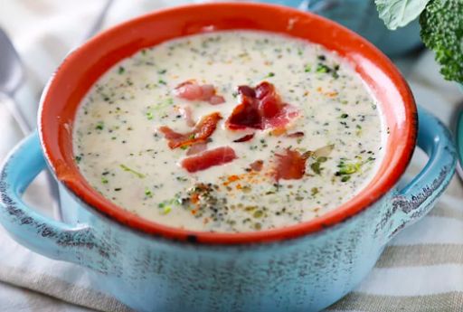 there is a bowl of soup with bacon and broccoli on the table next to it