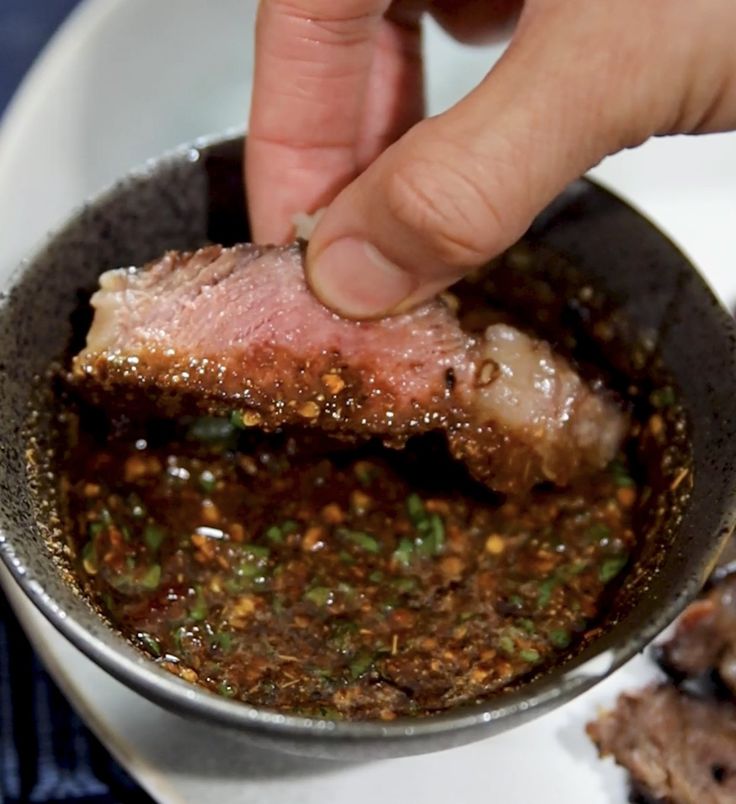 a person is dipping some meat into a bowl with other food on the plate in front of them