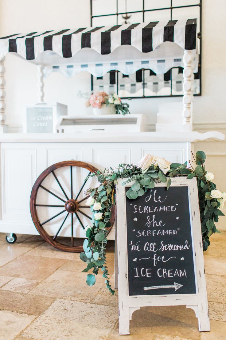 a chalkboard sign with flowers and greenery stands in front of an ice cream stand