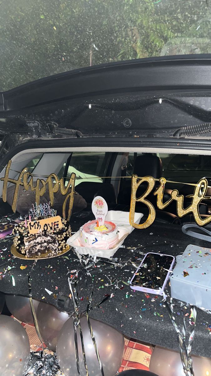 a birthday cake sitting in the back of a car with balloons and confetti