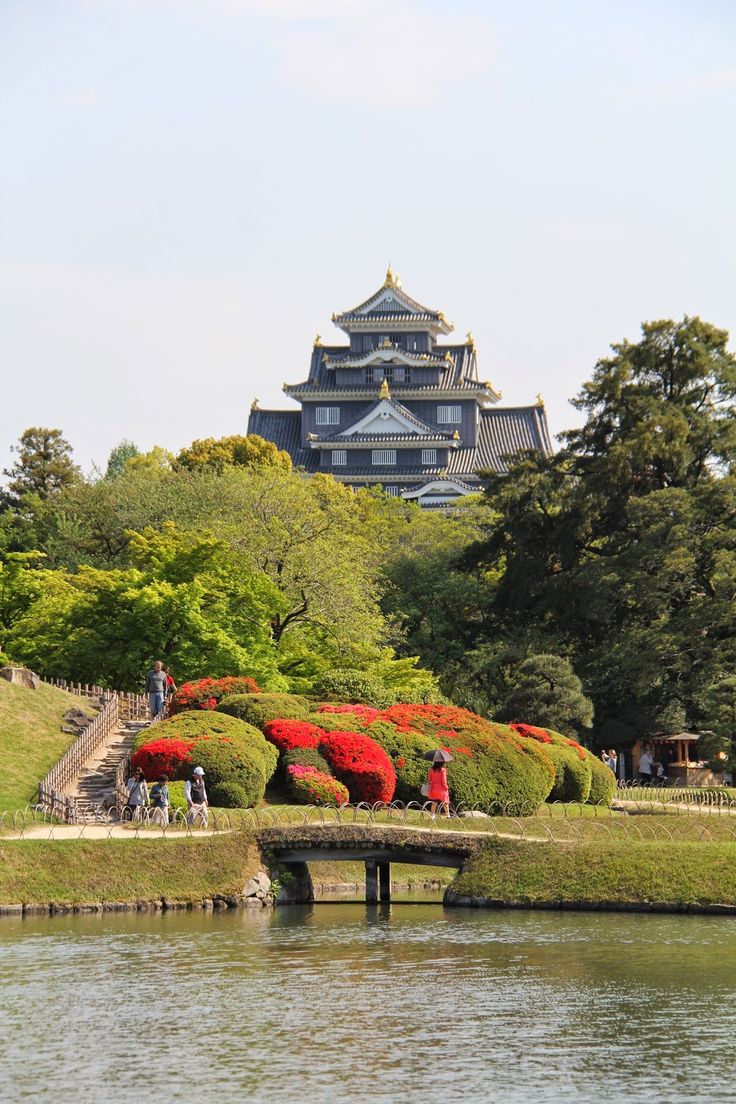 people are walking around in front of a building with red flowers on the ground and trees