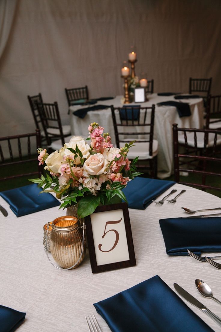 the table is set with blue napkins, silverware and flowers in a vase