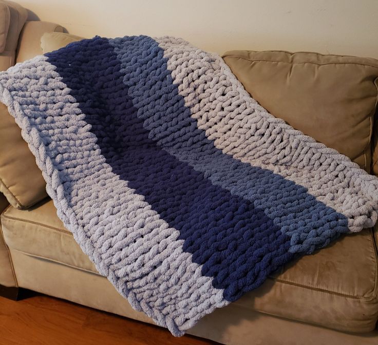 a blue and white crocheted blanket sitting on top of a couch next to a pillow