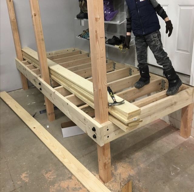 a young boy standing on top of a wooden bed frame in a room under construction