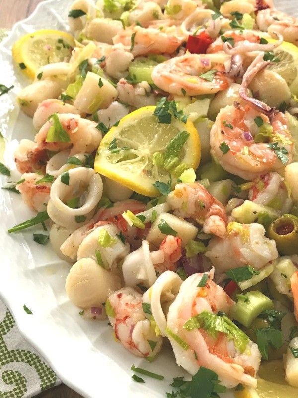 a white plate topped with shrimp and pasta salad next to lemon wedges on a wooden table