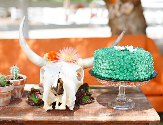 a table topped with a cake covered in green frosting next to a cow skull