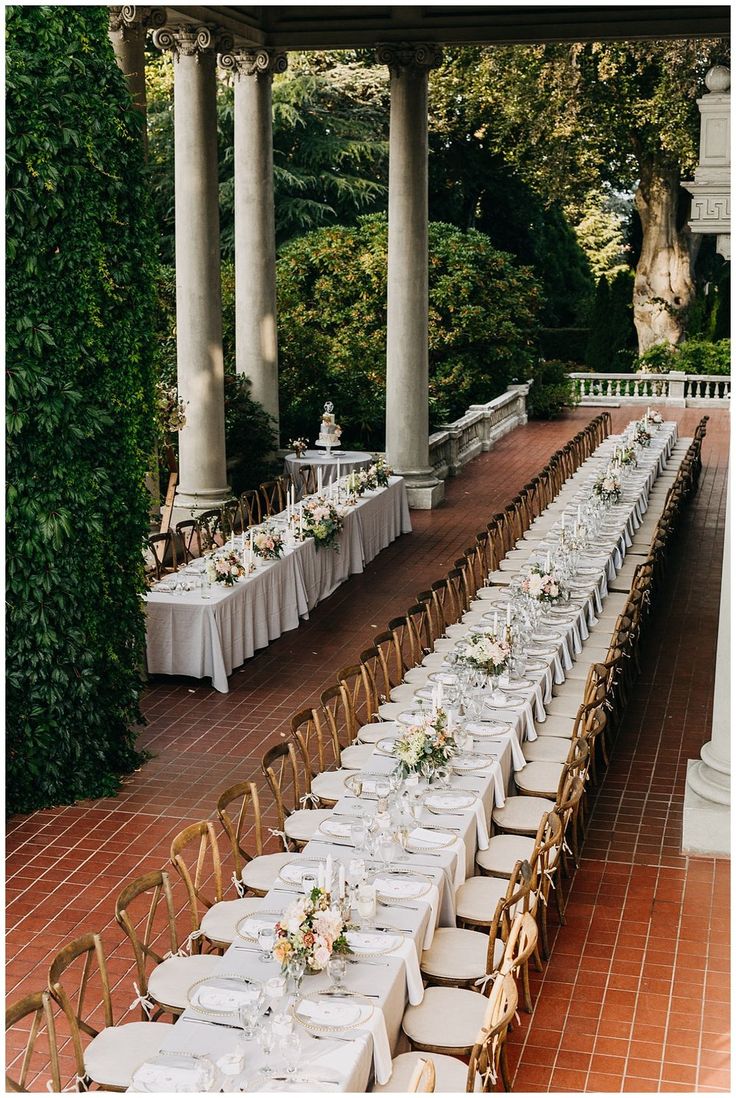 a long table set up with white linens and place settings for an outdoor wedding