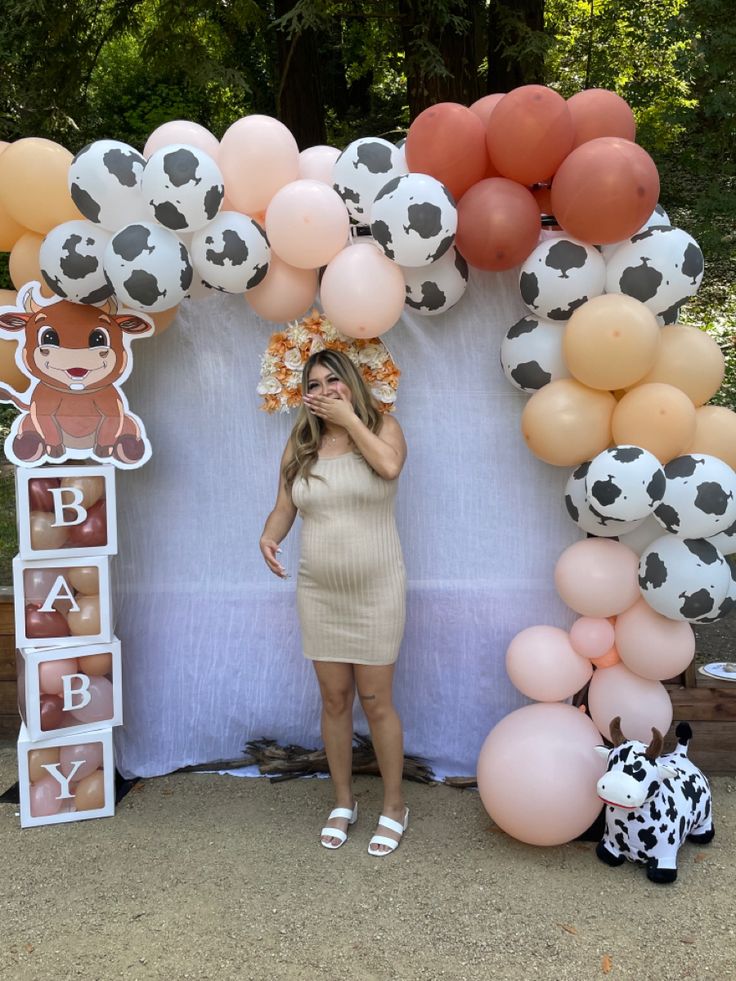 a woman standing in front of a backdrop made out of balloons and cow head decorations