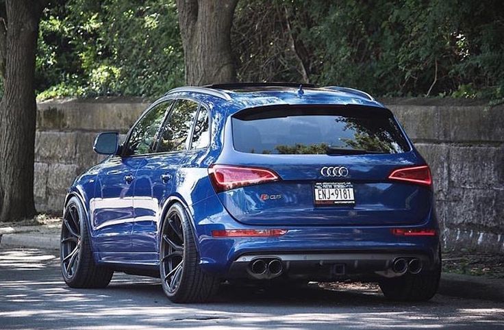 the rear end of a blue car parked in front of some trees on a street