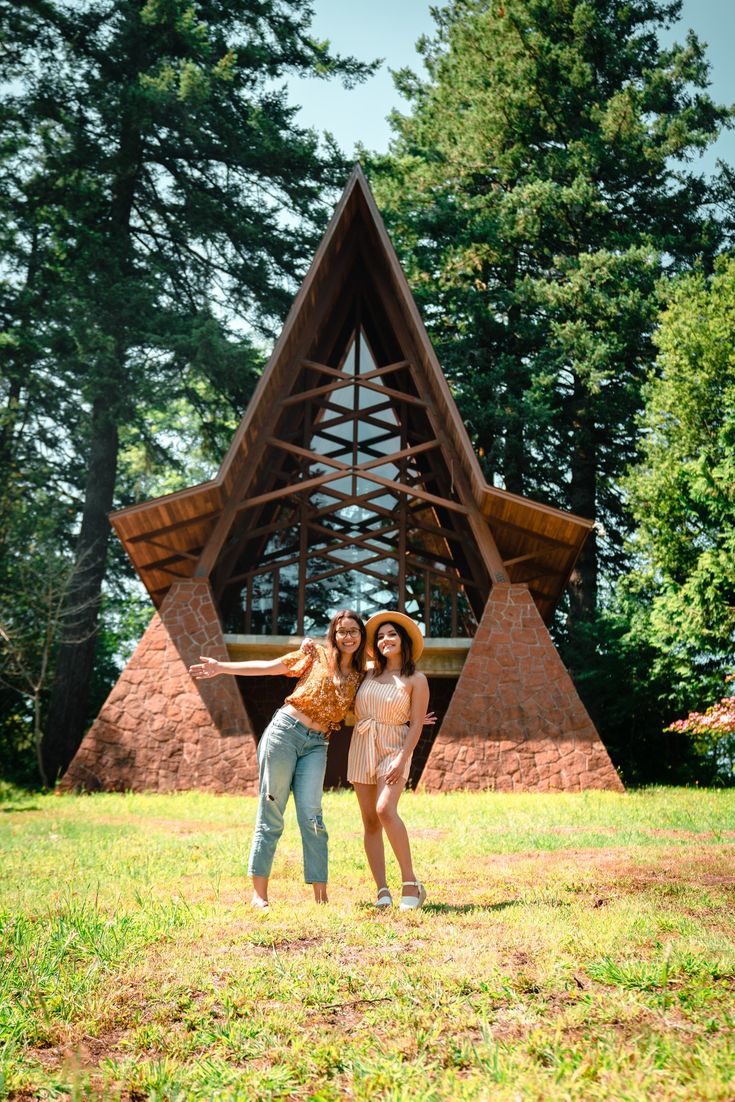 two women standing in front of a wooden structure with triangular shapes on it's sides