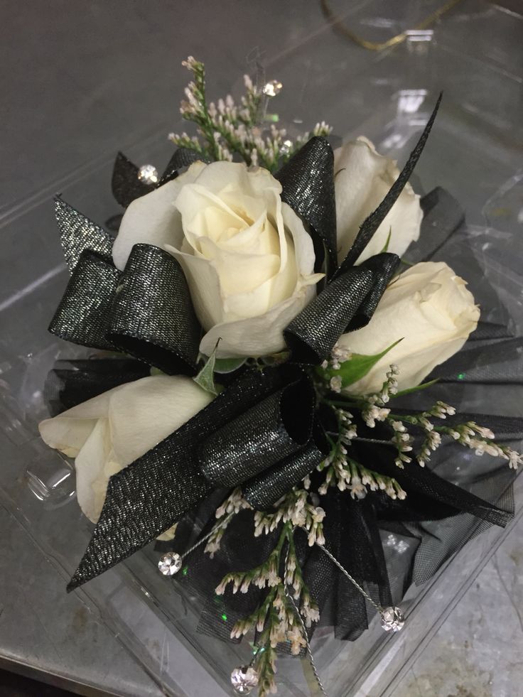 a bouquet of white roses sitting on top of a clear box with black ribbon around it