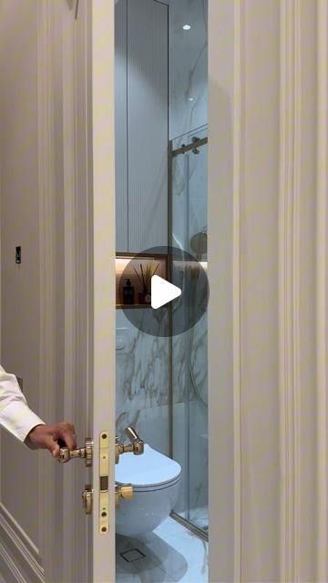 a man opening the door to a bathroom with a white toilet and glass shower stall