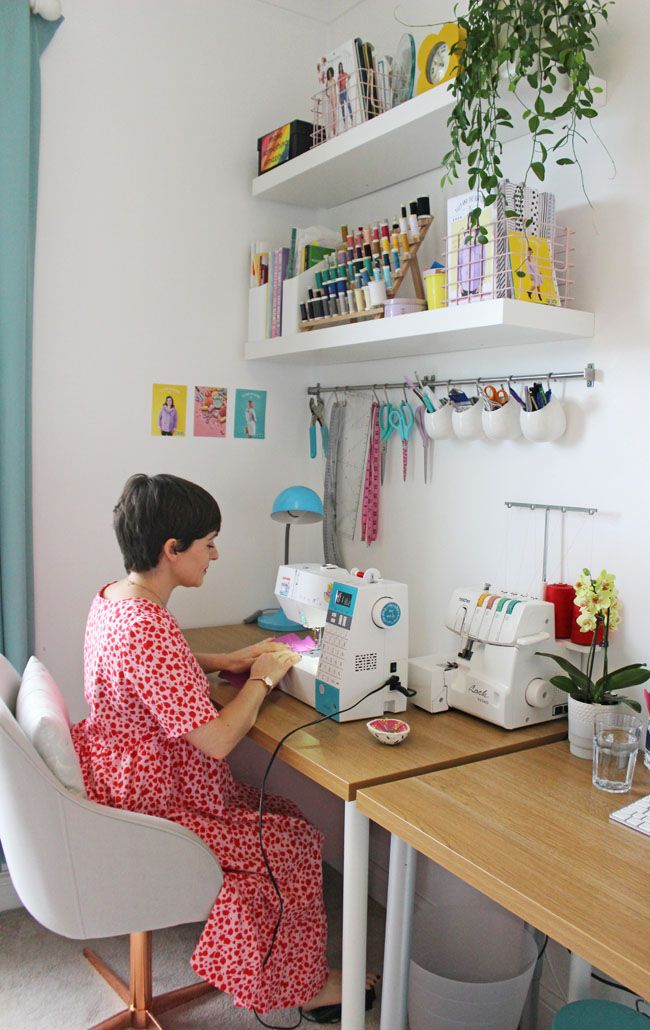 a woman sitting at a sewing machine in front of a desk with a plant on it