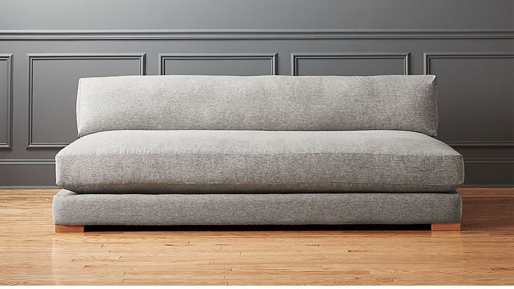 a grey couch sitting on top of a hard wood floor next to a gray wall