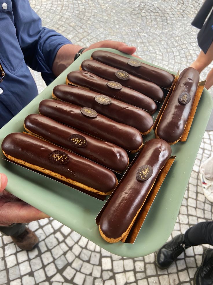 there is a tray full of chocolate covered doughnuts on the table and someone holding it