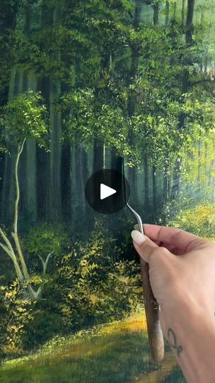 a person holding a spoon in front of a painting with trees and grass on it