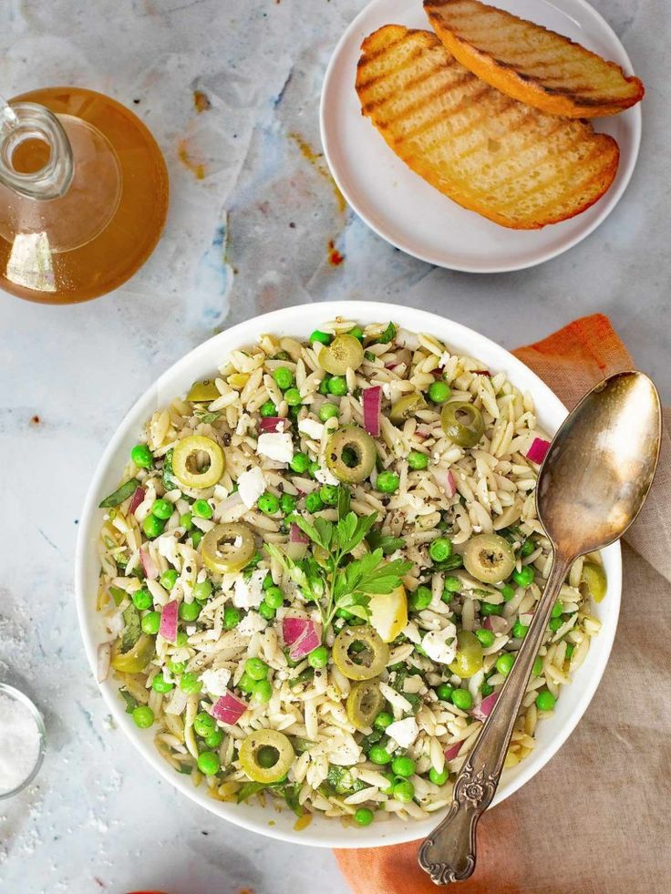 a bowl of pasta with peas, olives and parmesan cheese on the side