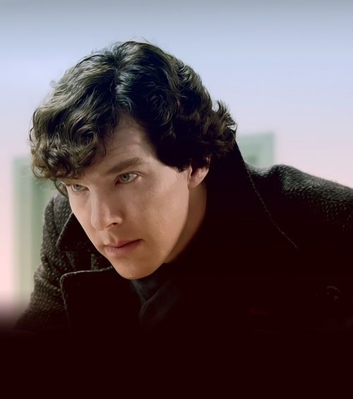 a man with curly hair wearing a black coat and looking off to the side in front of a cityscape