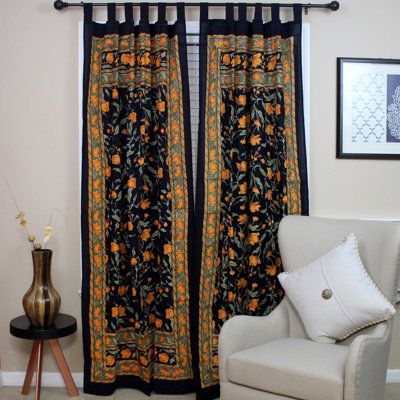 a white chair sitting in front of a window covered in black and orange floral curtains