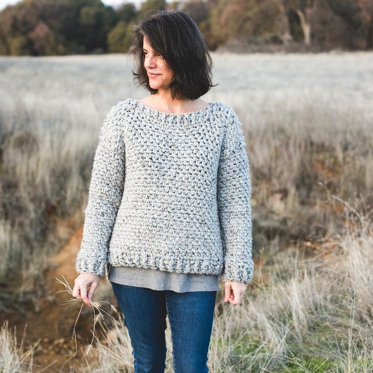 a woman standing in a field wearing a sweater