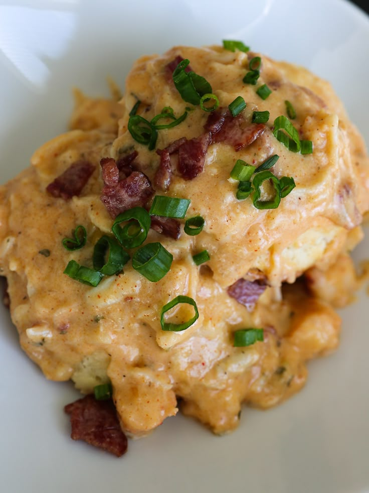 a white plate topped with cheesy potatoes covered in bacon and green onion garnish