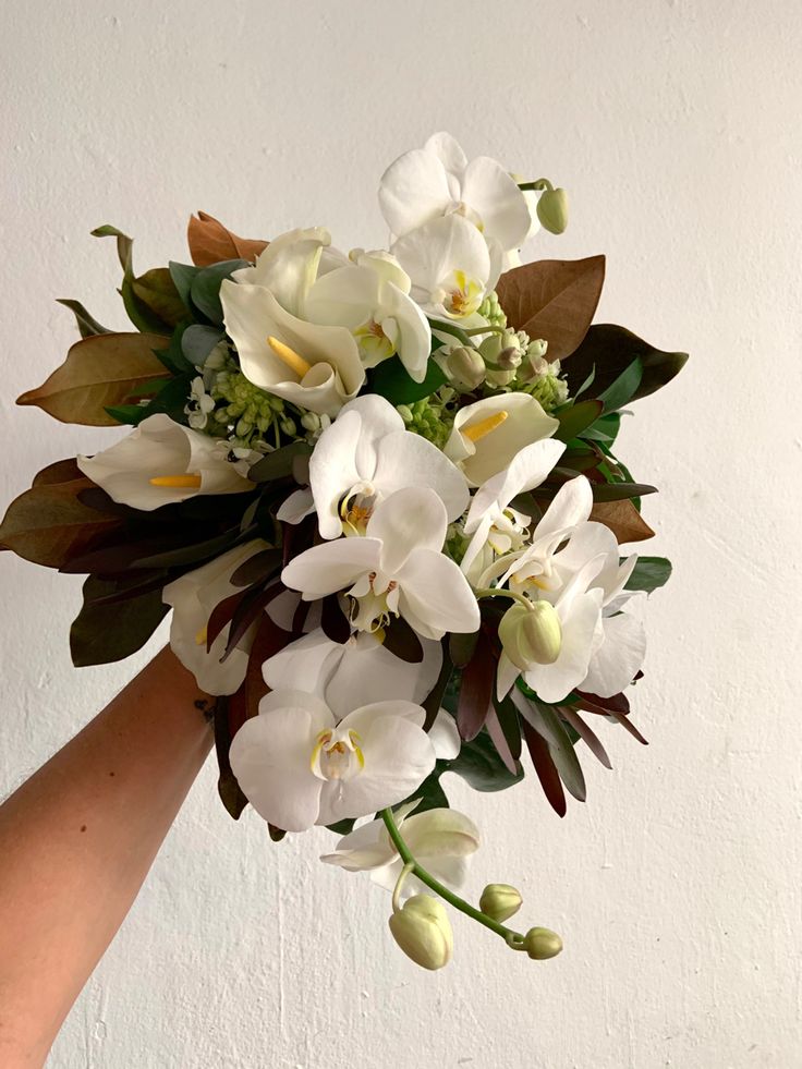 a bouquet of white flowers is held by someone's hand in front of a wall