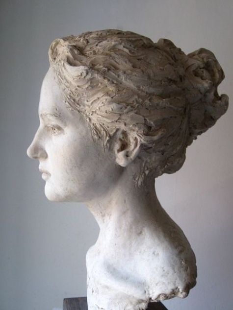 a statue of a woman's head with braids in her hair, against a white wall