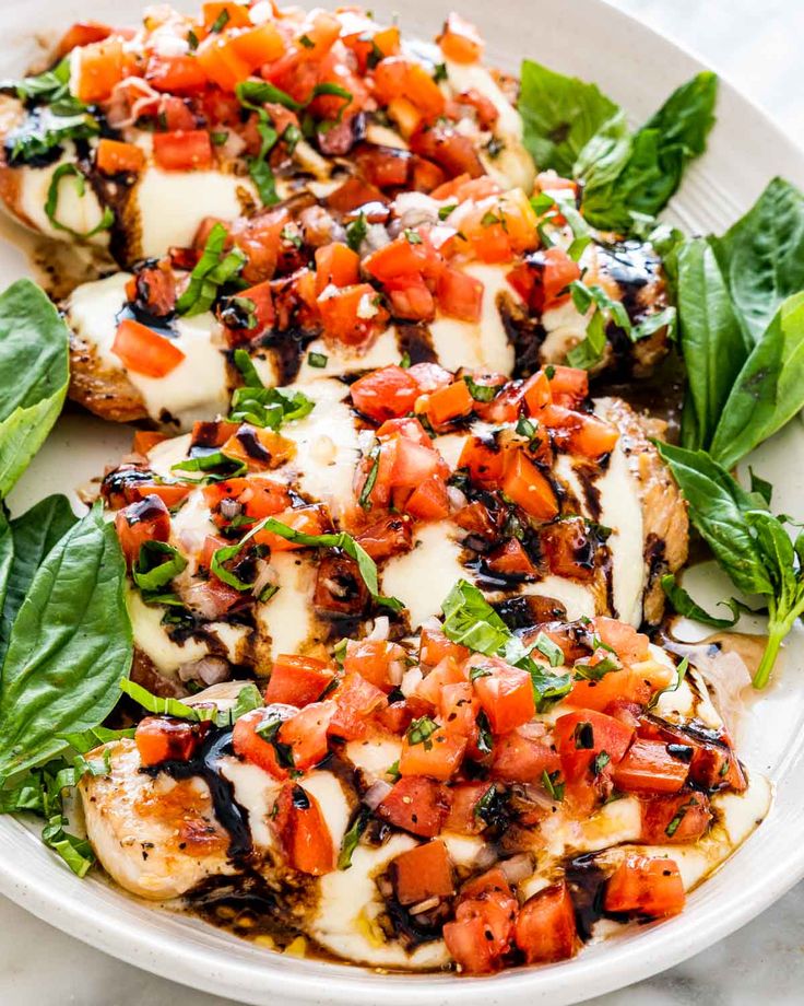 grilled chicken topped with tomatoes, cheese and spinach leaves on a white plate