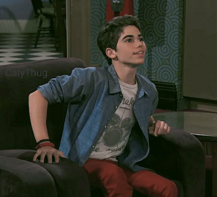 a young man sitting on top of a black chair in front of a tv screen