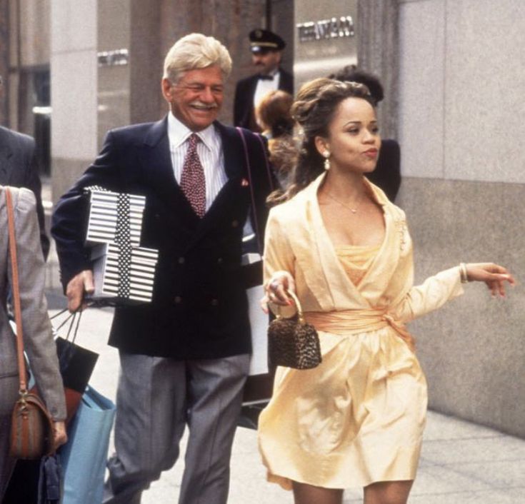 a woman in a yellow dress walking down the street next to a man wearing a suit and tie