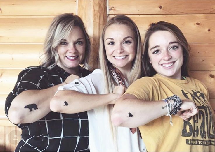 three women standing next to each other in front of a wooden wall with tattoos on their arms