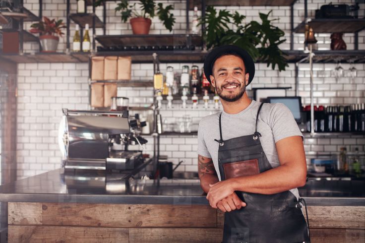 a man in an apron is standing at the counter with his arms crossed and smiling