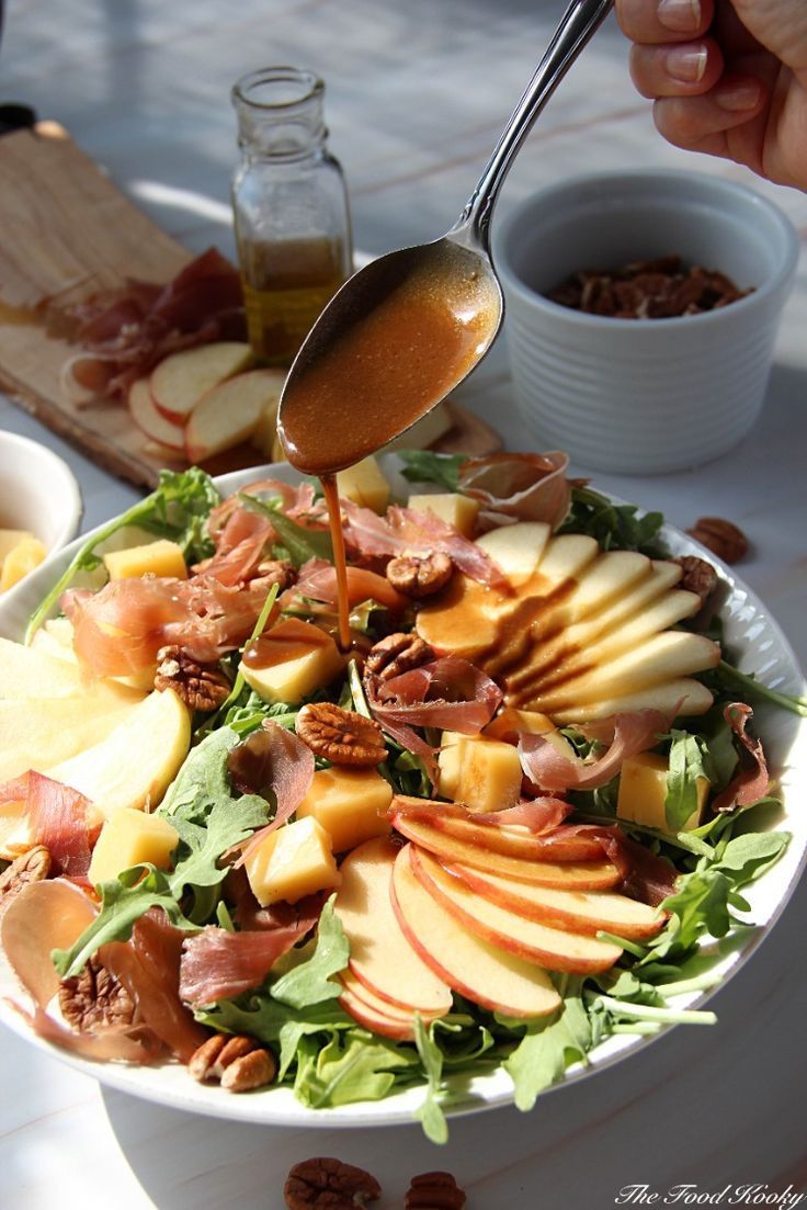 a person pouring dressing onto a salad with apples and nuts