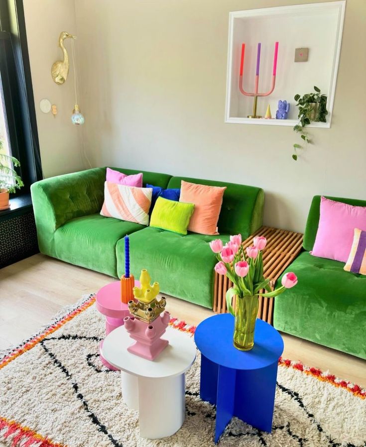 a living room filled with green couches and colorful tables in front of a window