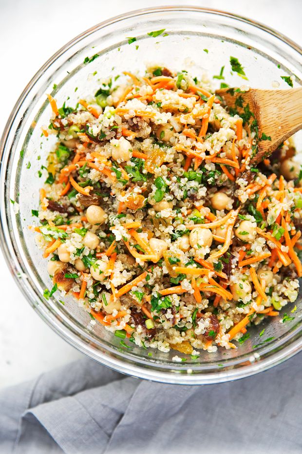 a glass bowl filled with carrots, couscous and other vegetables next to a wooden spoon