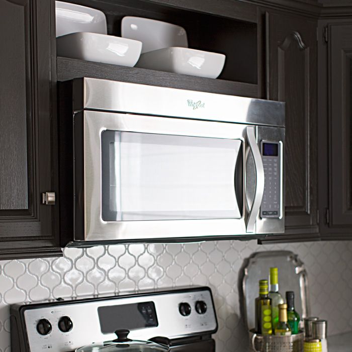 a stainless steel stove and microwave in a kitchen with dark wood cabinets, white marble countertops and gray backsplash