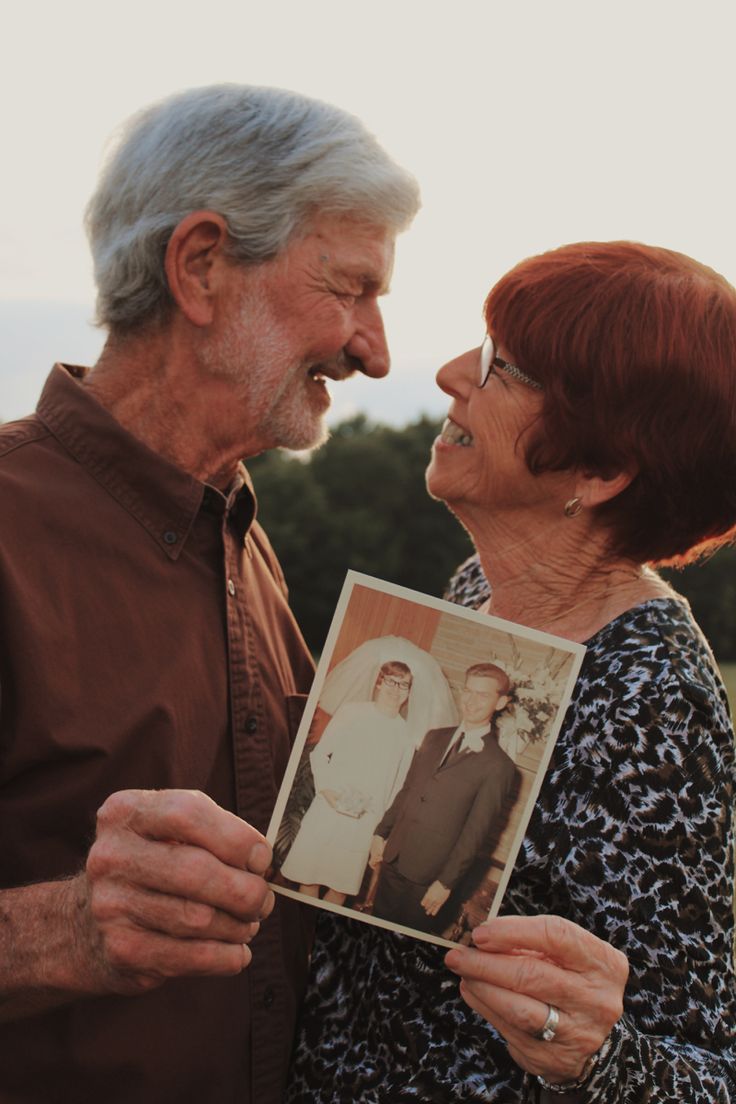 an older man and woman standing next to each other holding up a picture with the image of them on it