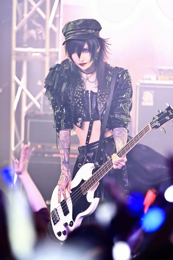 a woman with black hair and piercings holding a white guitar in front of a crowd