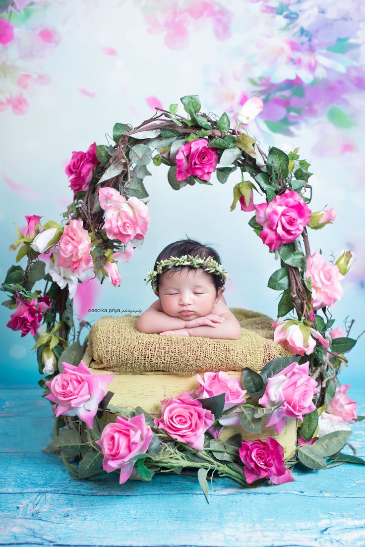 a baby is laying down in a basket with pink flowers around it and surrounded by greenery