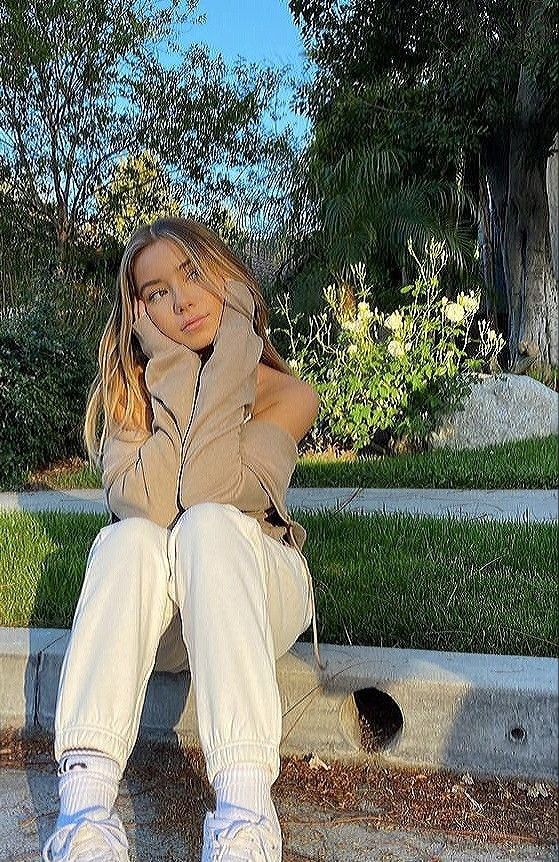 a woman sitting on the curb with her hands behind her head and looking at the camera