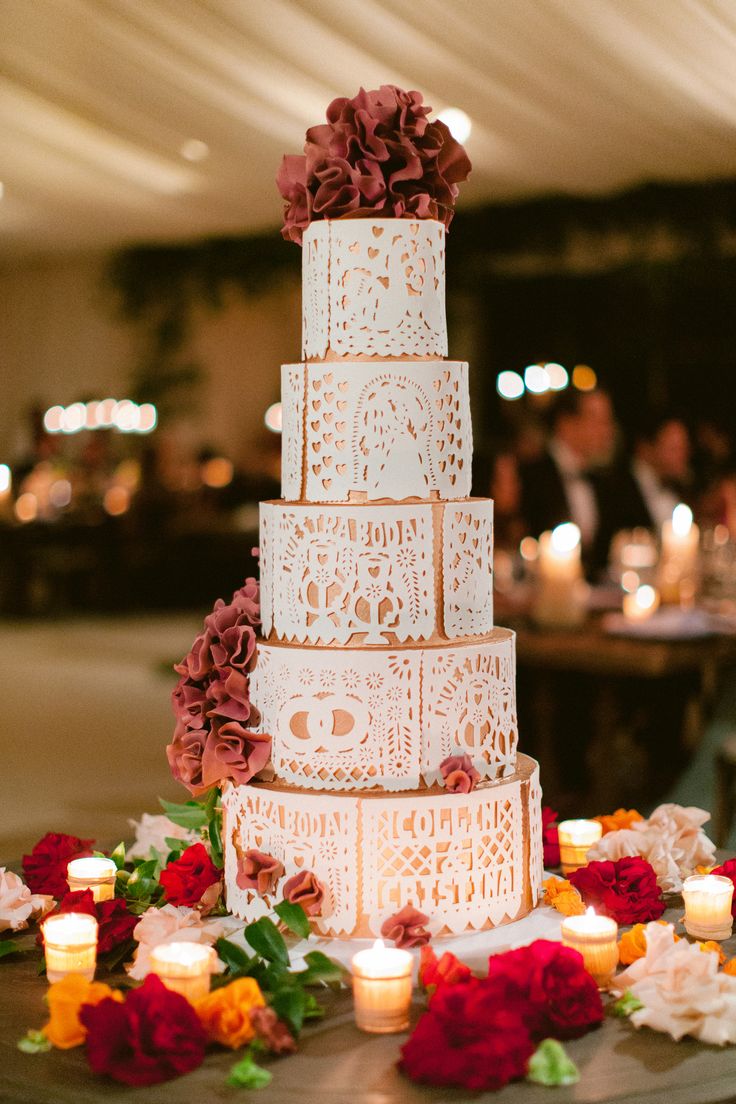 a three tiered wedding cake with flowers and candles on the table next to it