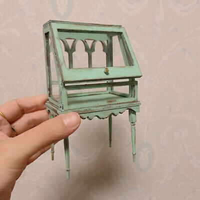 a miniature green desk and chair in someone's hand on a wallpapered background