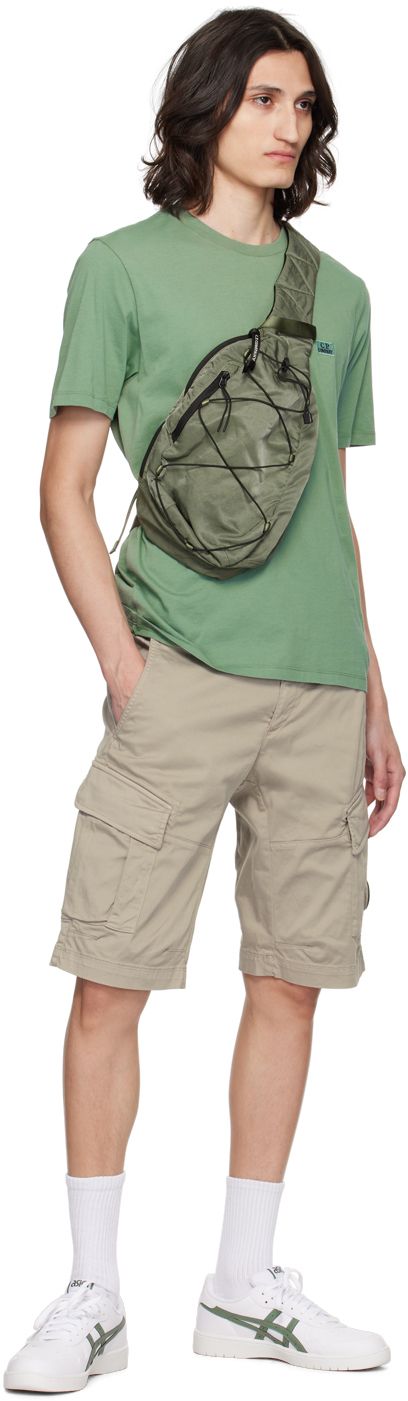 Water-resistant garment-dyed nylon sateen messenger bag in green. · Webbing carry handle · Zip pocket at press-release crossbody strap · Logo-printed acetate lens · Zip pocket at face · Criss-crossing bungee-style drawstring · Padded mesh back face · Zip closure · Patch pockets and lanyard clasp at interior · Canvas lining · H13.5 x W10 x D3.5 Supplier color: Agave green Streetwear Nylon Bag With Side Pockets, Nylon Bags For Streetwear, Casual Green Bags With Functional Pockets, Urban Green Bag With Pockets, Casual Green Shoulder Bag With Functional Pockets, Green Utility Bags With Pockets, Green Utility Bag With Pockets, Green Utility Shoulder Bag For Outdoor, Green Nylon Bag With Multiple Pockets