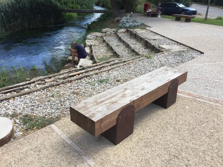 a wooden bench sitting on top of a sidewalk next to a river and train tracks