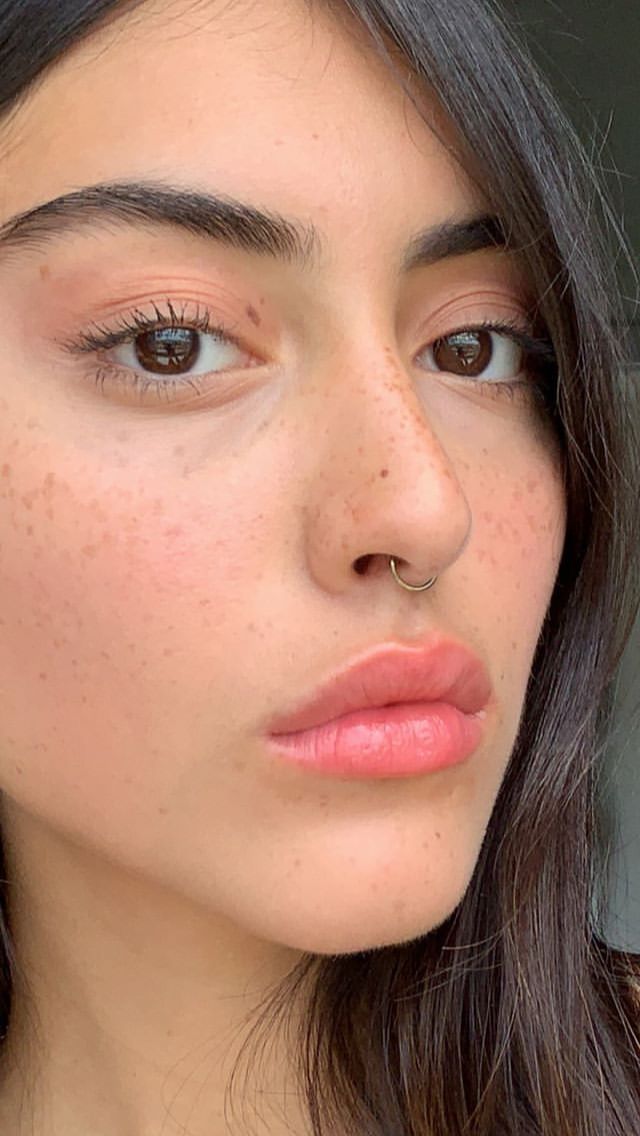 a woman with freckles on her face is looking at the camera and she has brown eyes