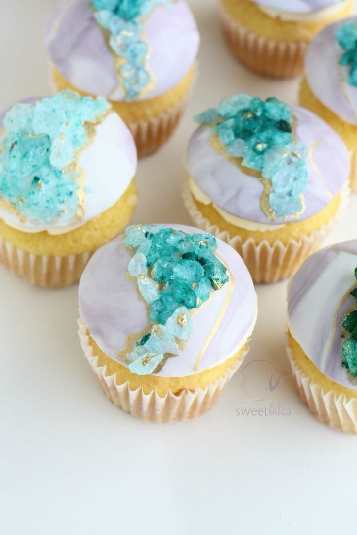 cupcakes with blue frosting and green sprinkles on white surface