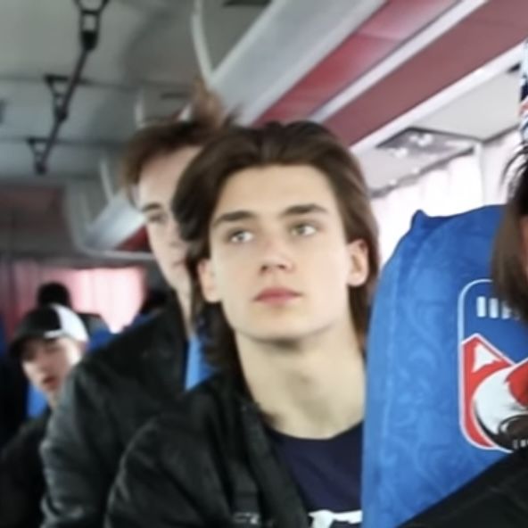 two young men sitting next to each other on a bus, one looking at the camera